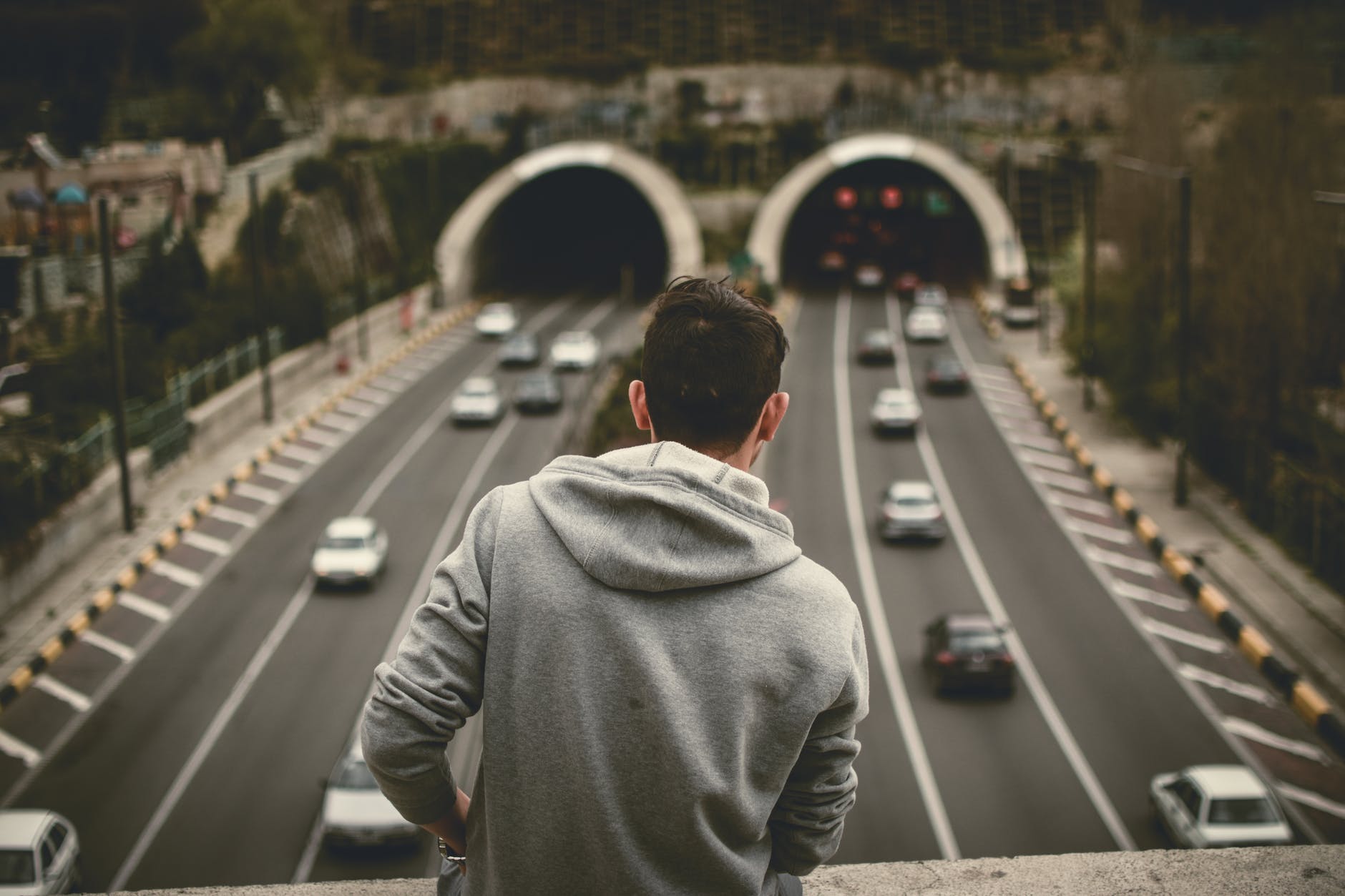 man in grey hoodie standing on bridge over the expressway