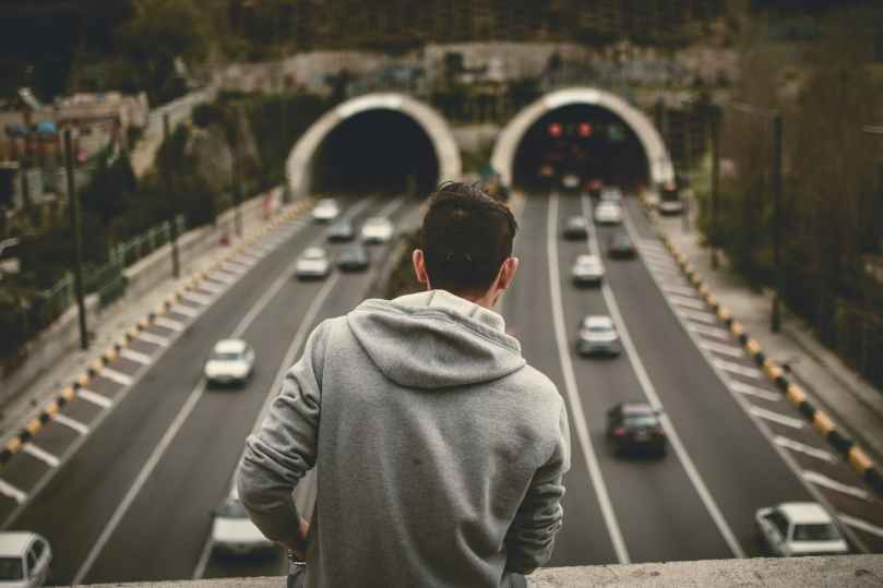man in grey hoodie standing on bridge over the expressway