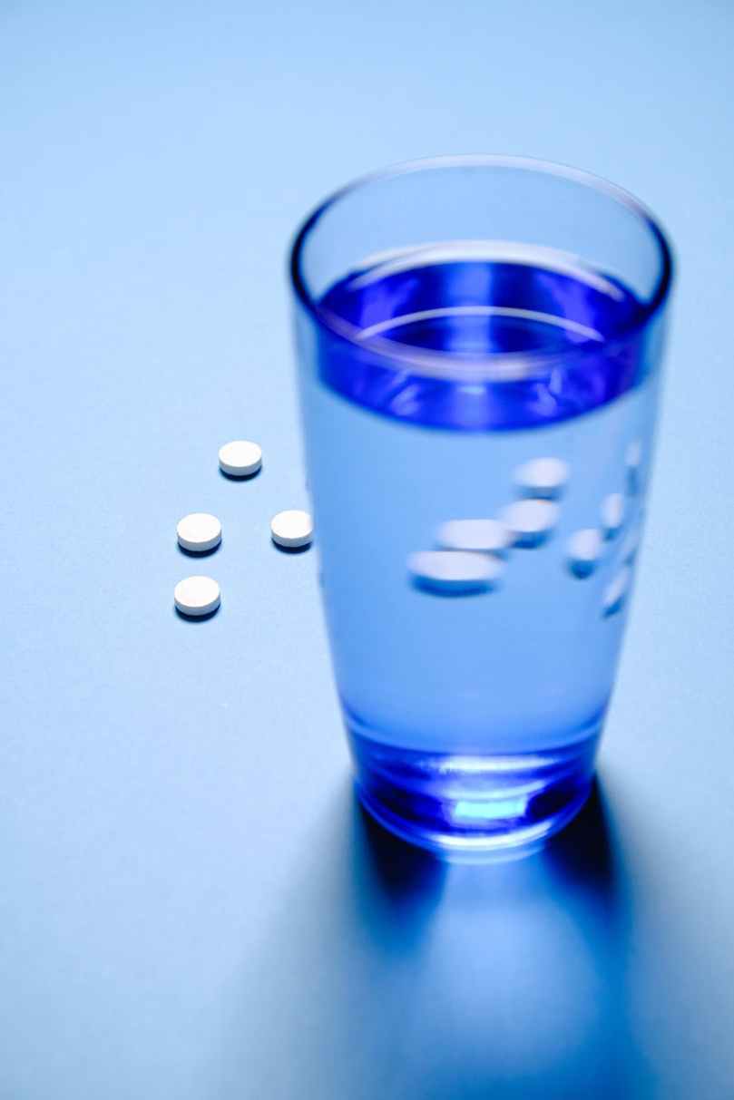 blue drinking glass with water and white medicine pills